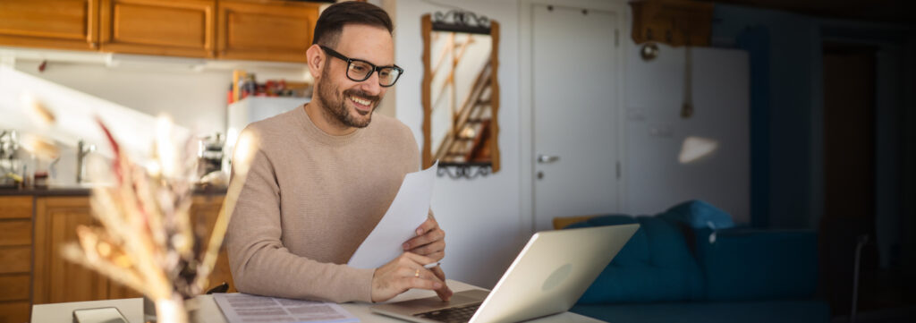 man on his laptop, with paper in hand.