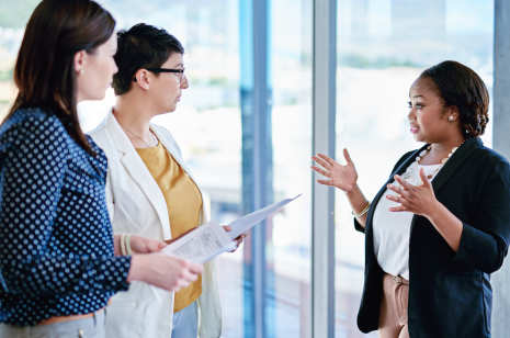 Three female professionals speaking in walkway.